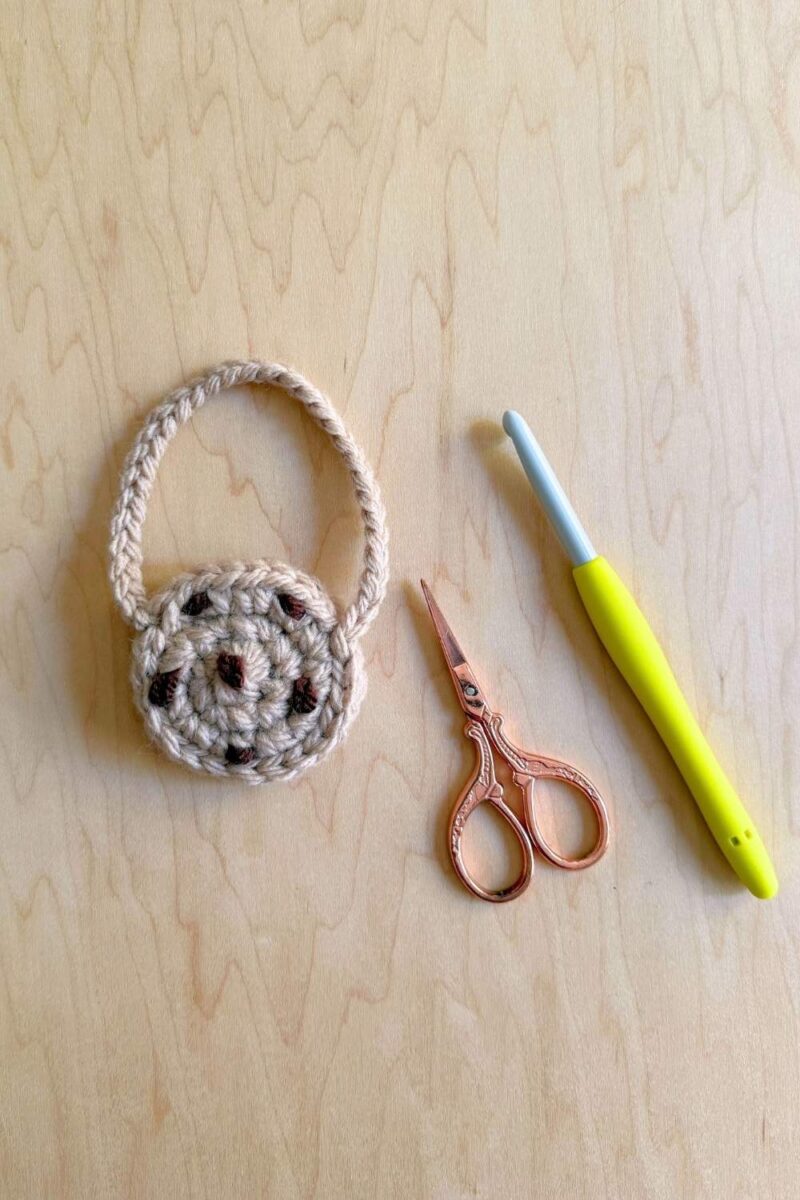 A photo showing the finished crochet cookie purse on a wood surface with scissors and crochet hook.
