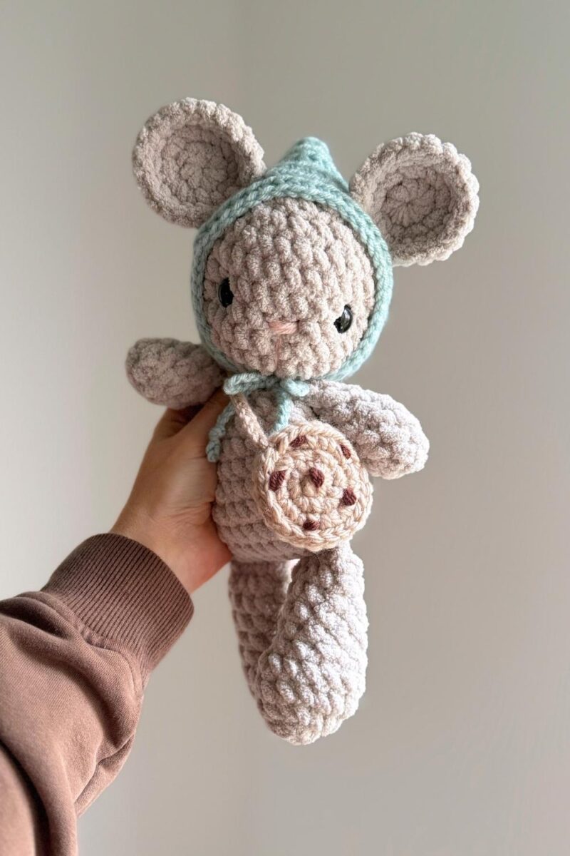 Hand holding a gray crochet mouse wearing a crochet cookie purse and blue pixie hat.