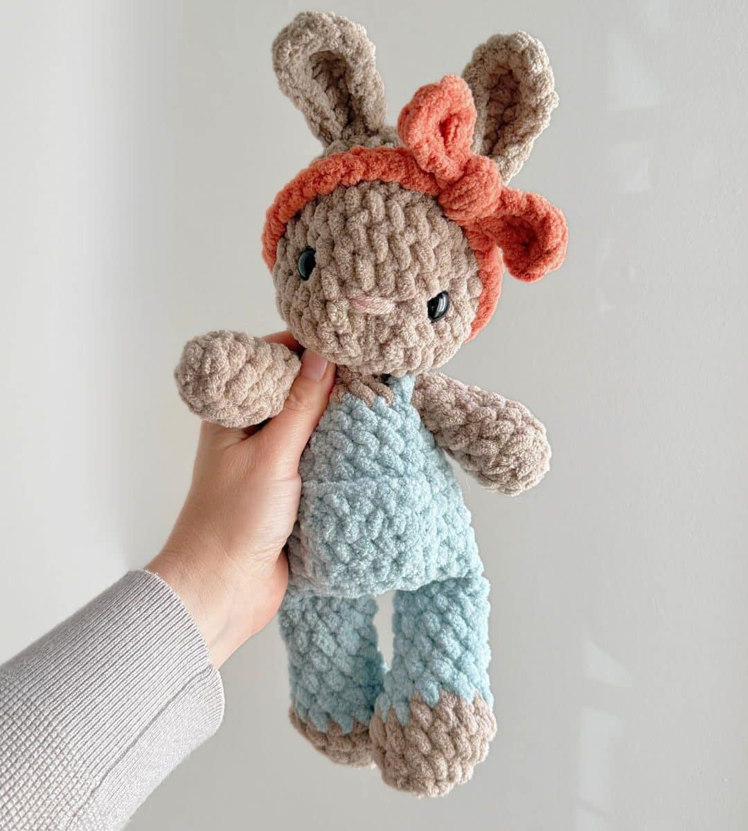 A brown Crochet Bunny in blue overalls with an orange headband.