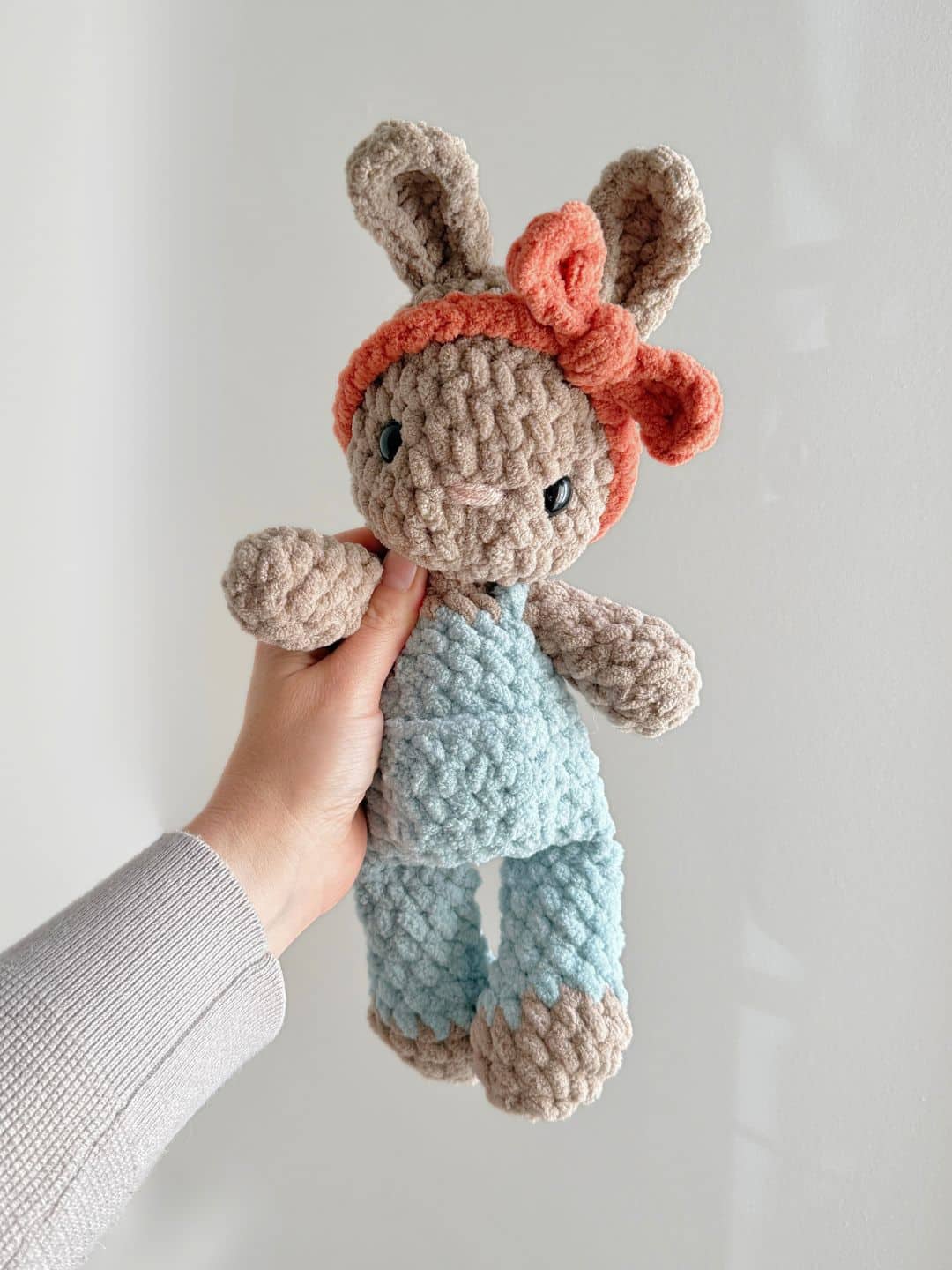 A brown Crochet Bunny in blue overalls with an orange headband.
