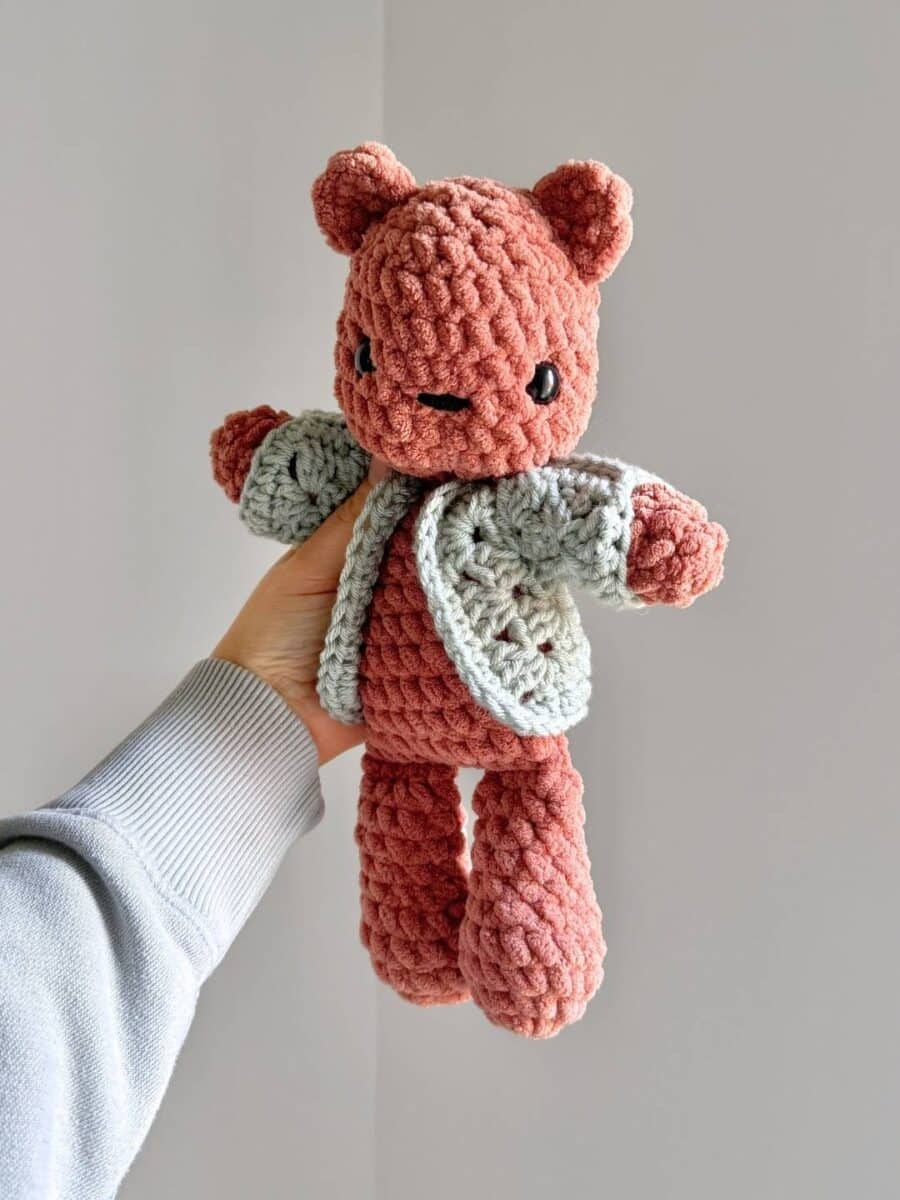 A brown crochet bear wearing a crochet sweater.