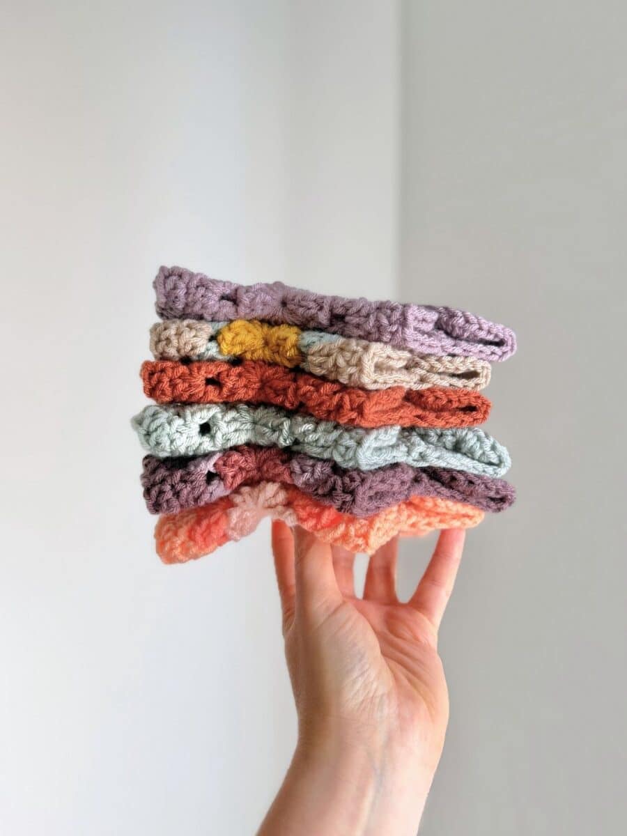 Hand holding a stack of tiny crochet cardigans in different colors.