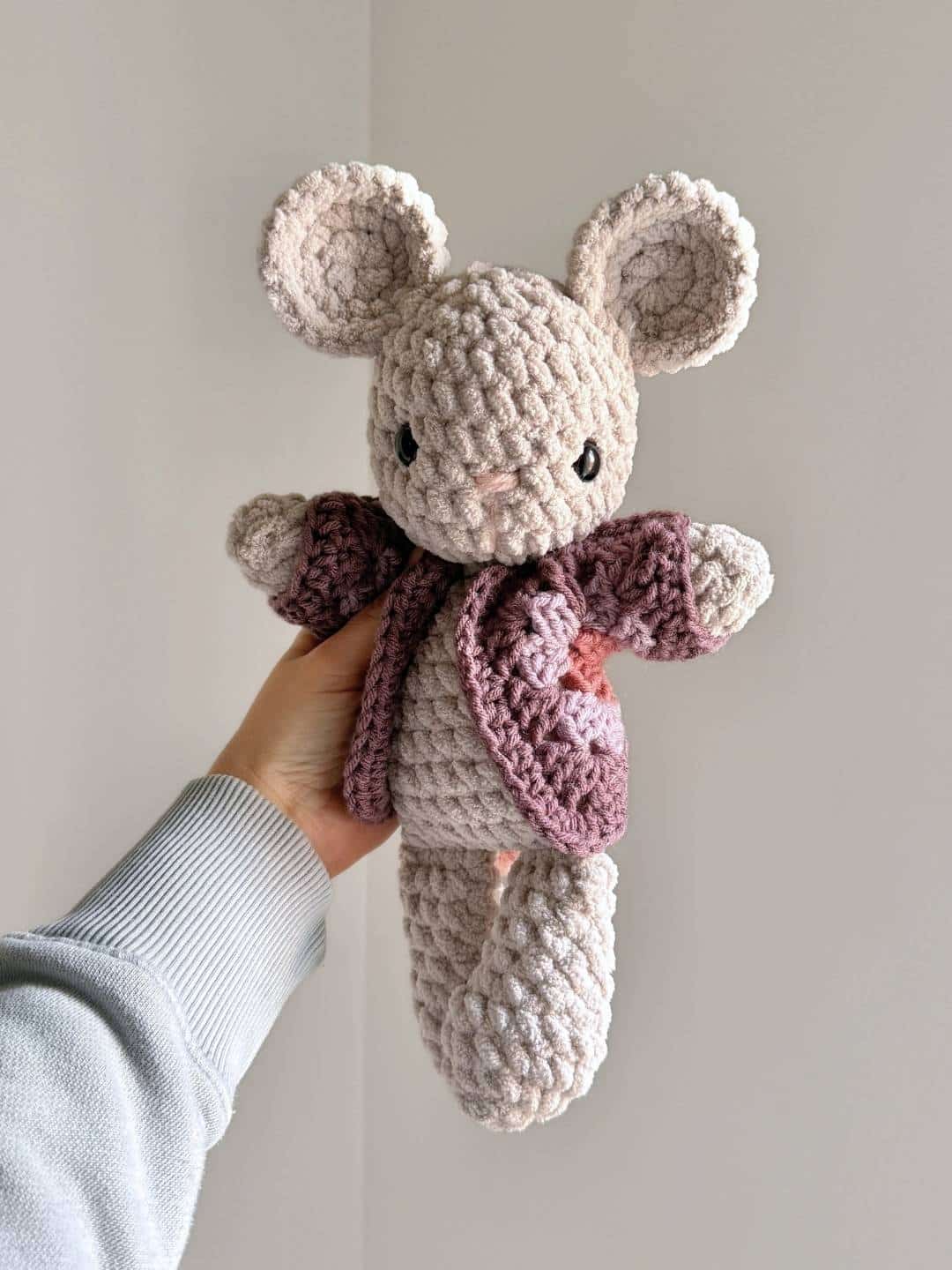 A gray crochet mouse wearing a multicolored purple crochet cardigan.